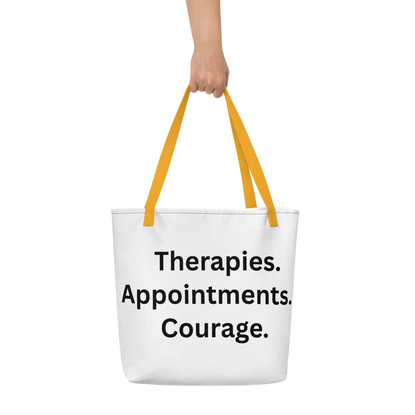 White tote bag with yellow handles and text 'Therapies. Appointments. Courage.' held by a person on a white background