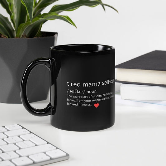 Black mug with text on a desk with a plant and books in the background