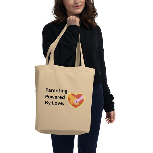 Person holding a beige tote bag with 'Parenting Powered By Love' text and heart design.