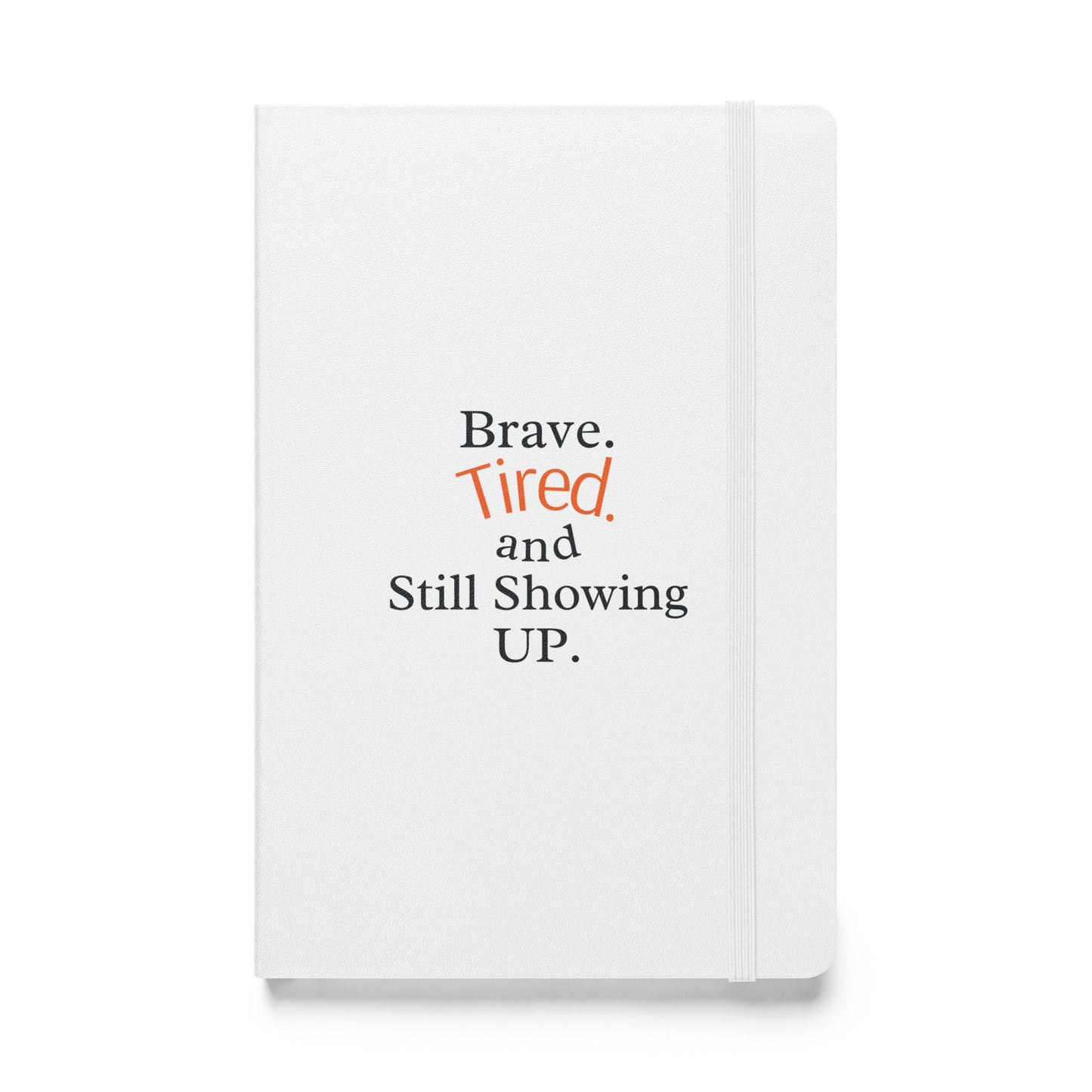 White notebook with text 'Brave. Tired. and Still Showing UP.' on a white background