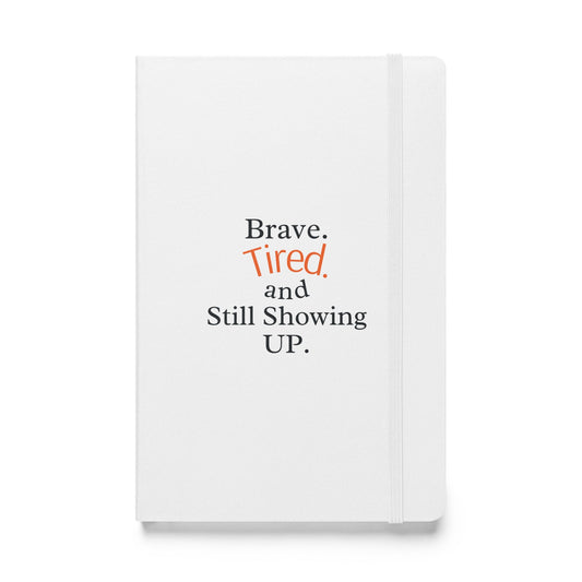 White notebook with text 'Brave. Tired. and Still Showing UP.' on a white background