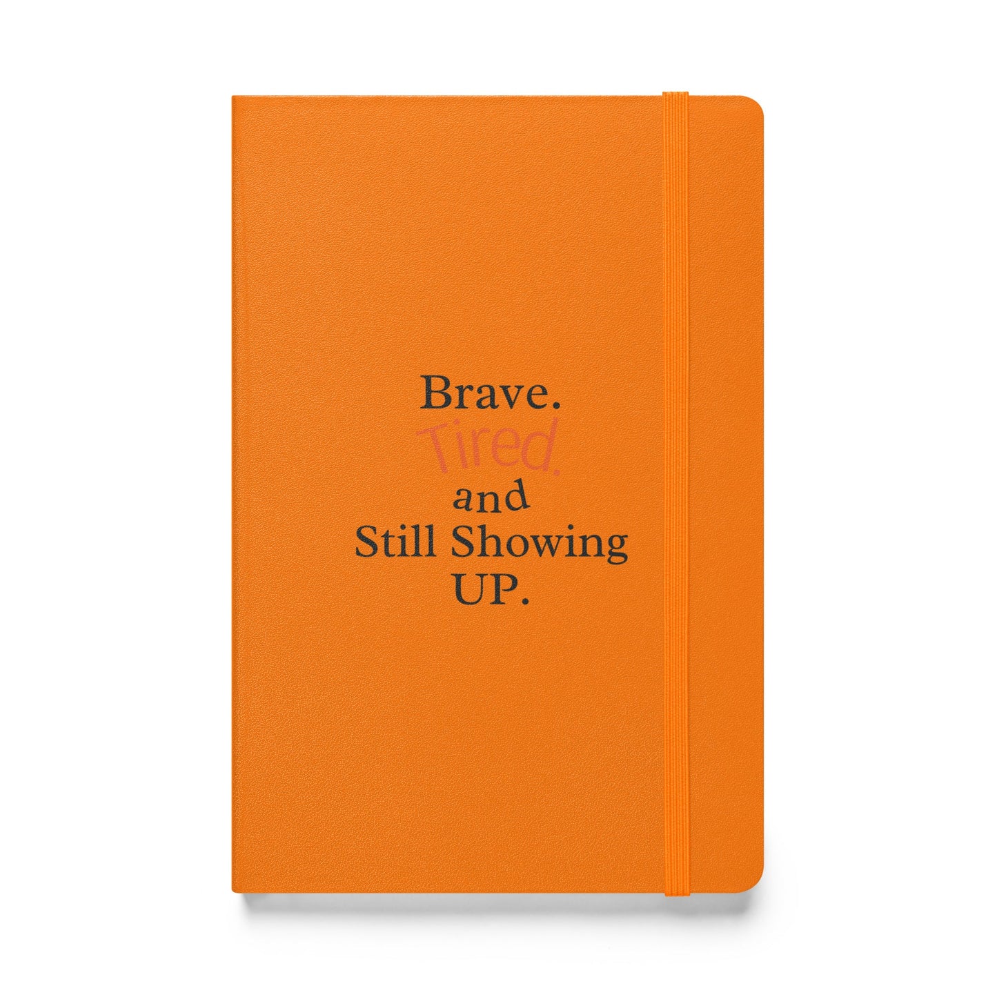 Orange notebook with text 'Brave. Tired and Still Showing UP.' on a white background