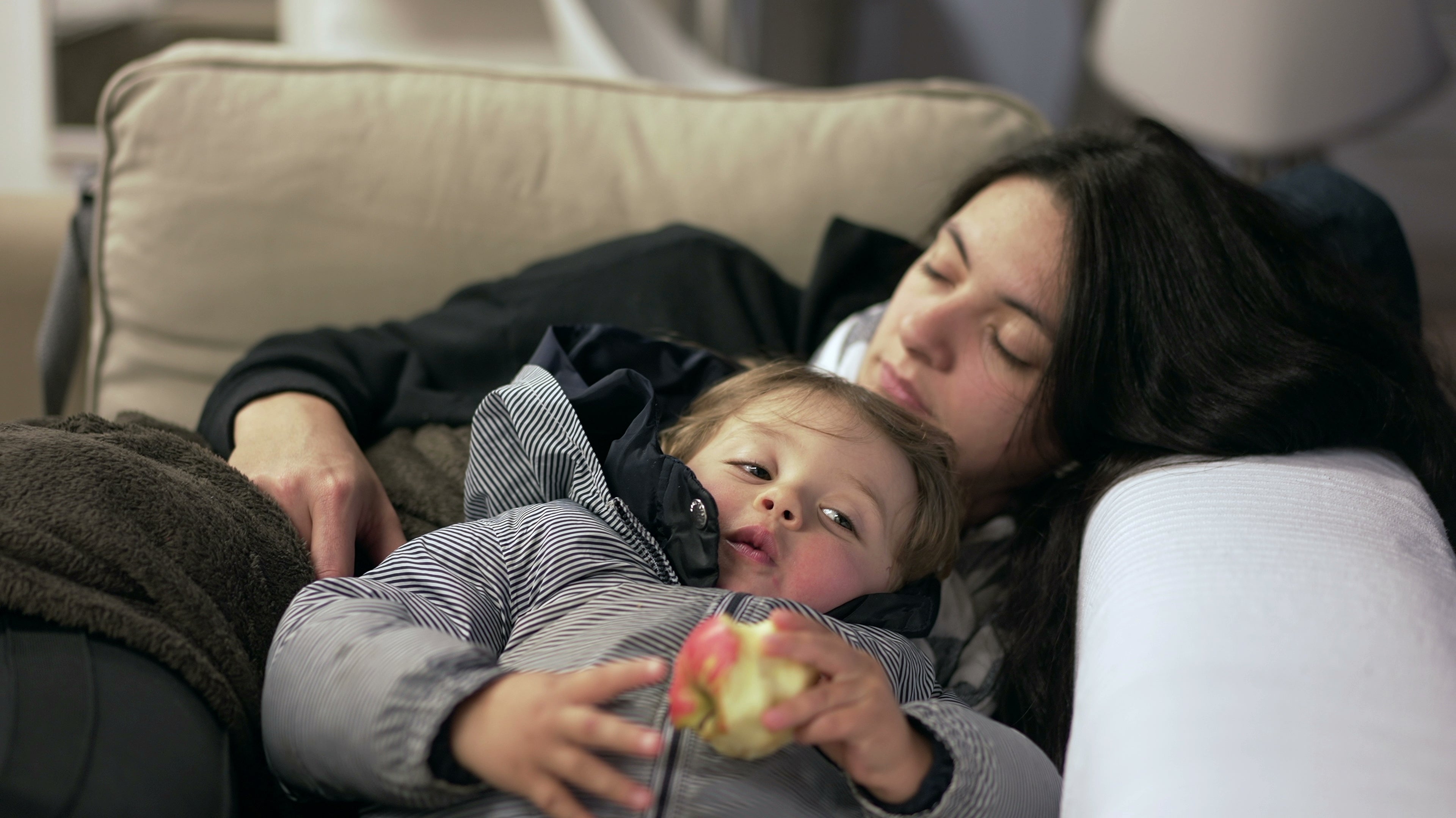 Woman and child sitting on a couch, with the child holding an apple.