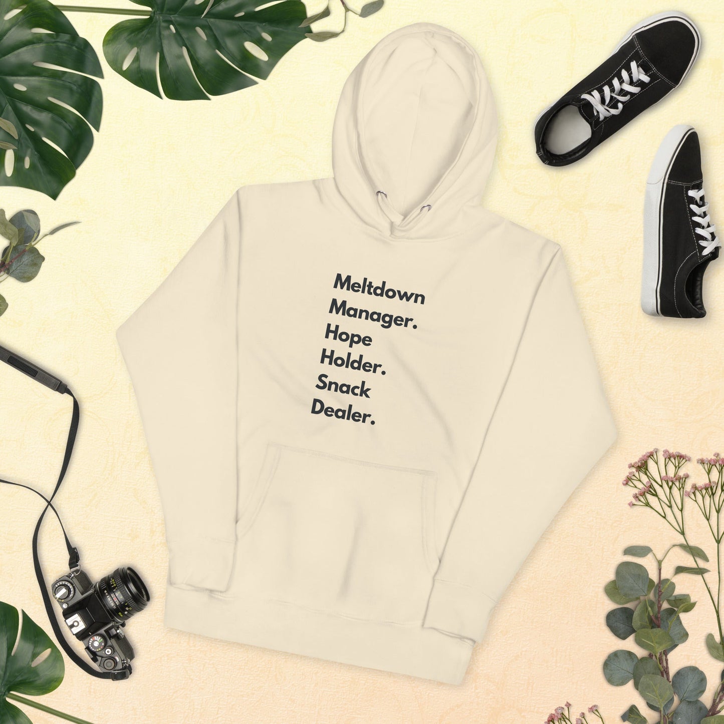 Beige hoodie with text, black sneakers, camera, and green leaves on a beige background