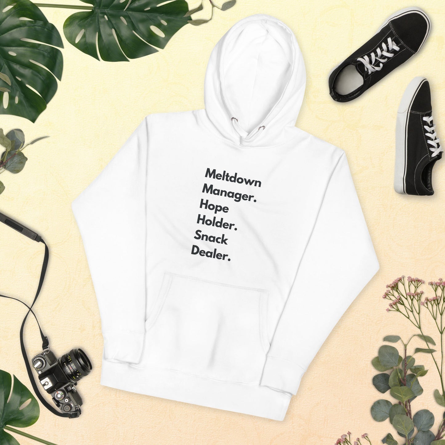 White hoodie with text, black sneakers, camera, and plants on a beige background