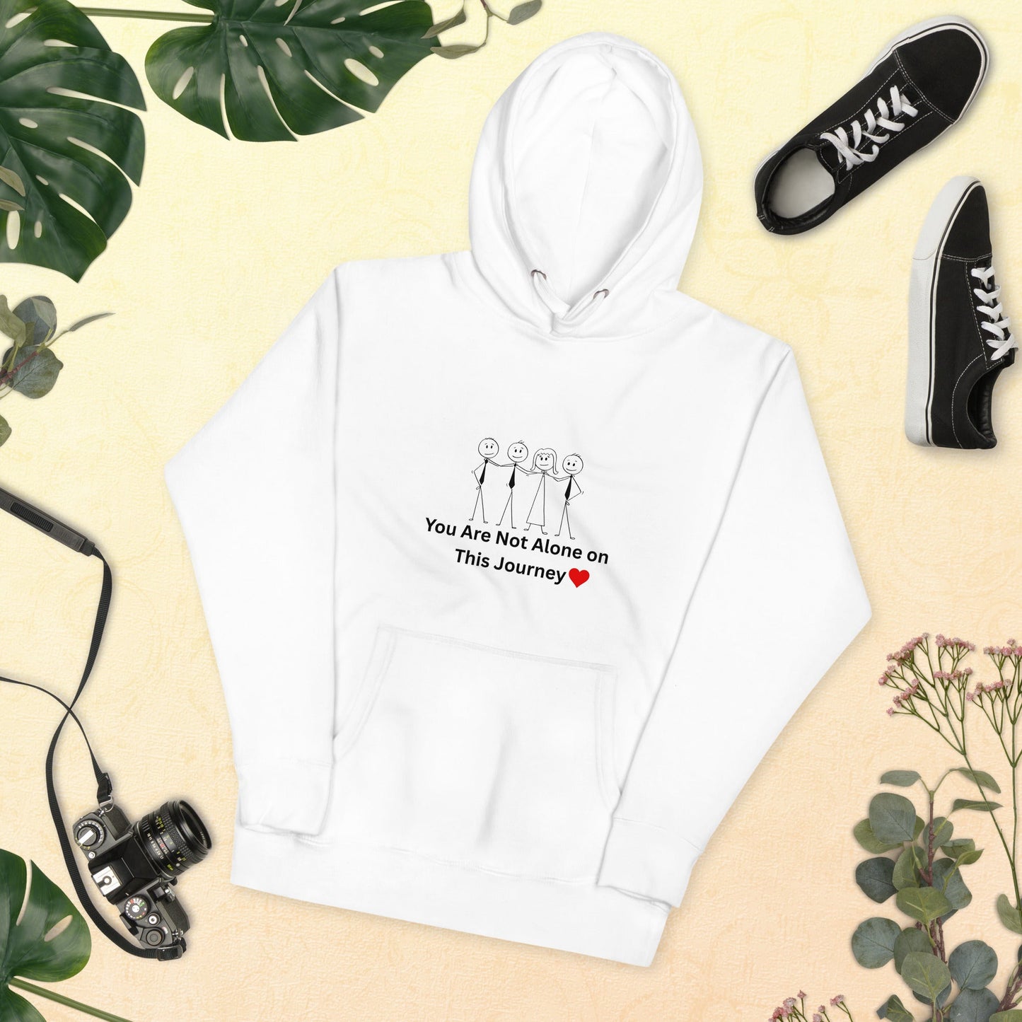 White hoodie with motivational text and graphics on a beige background with shoes and plants.