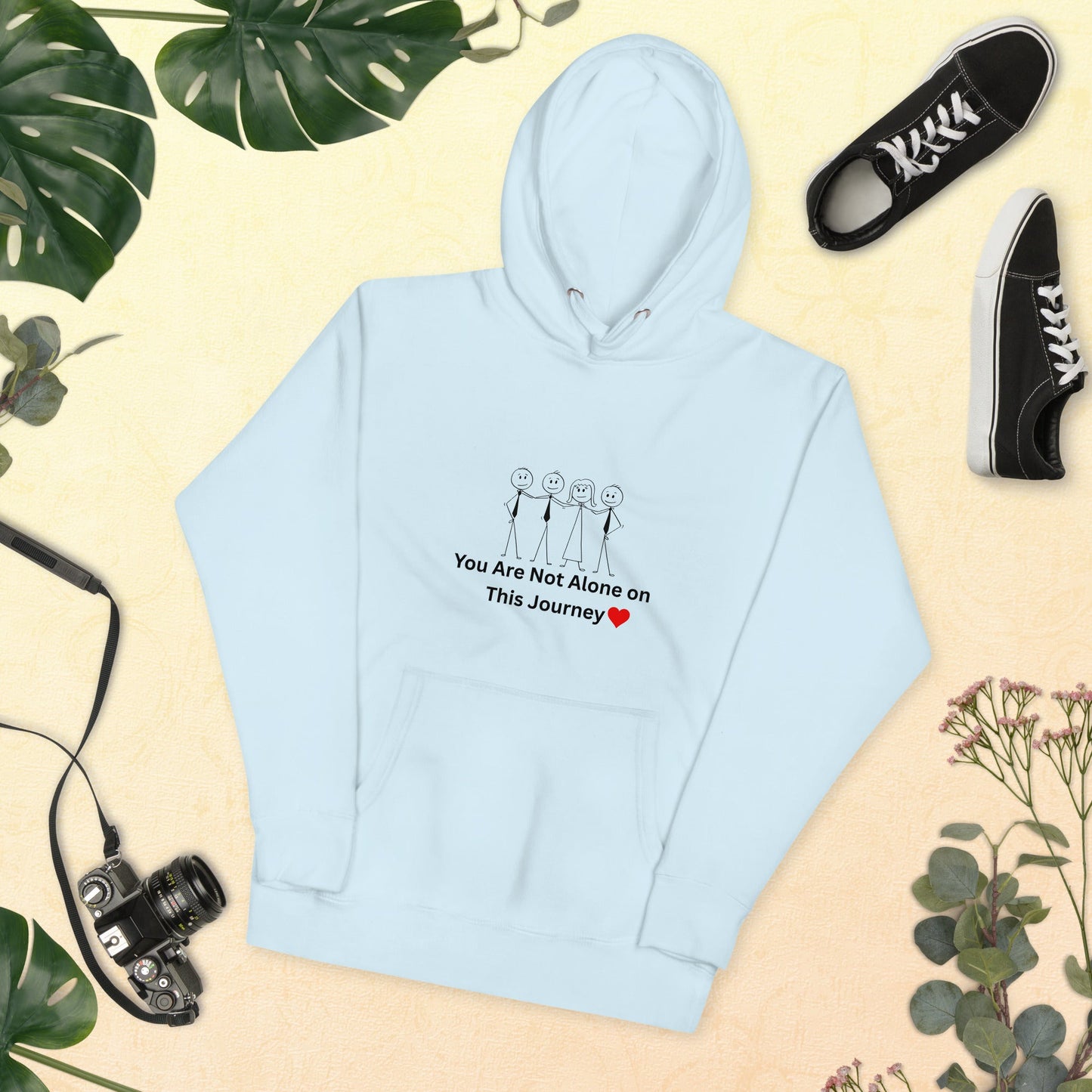 Light blue hoodie with text and graphics on a beige background with plants and shoes.