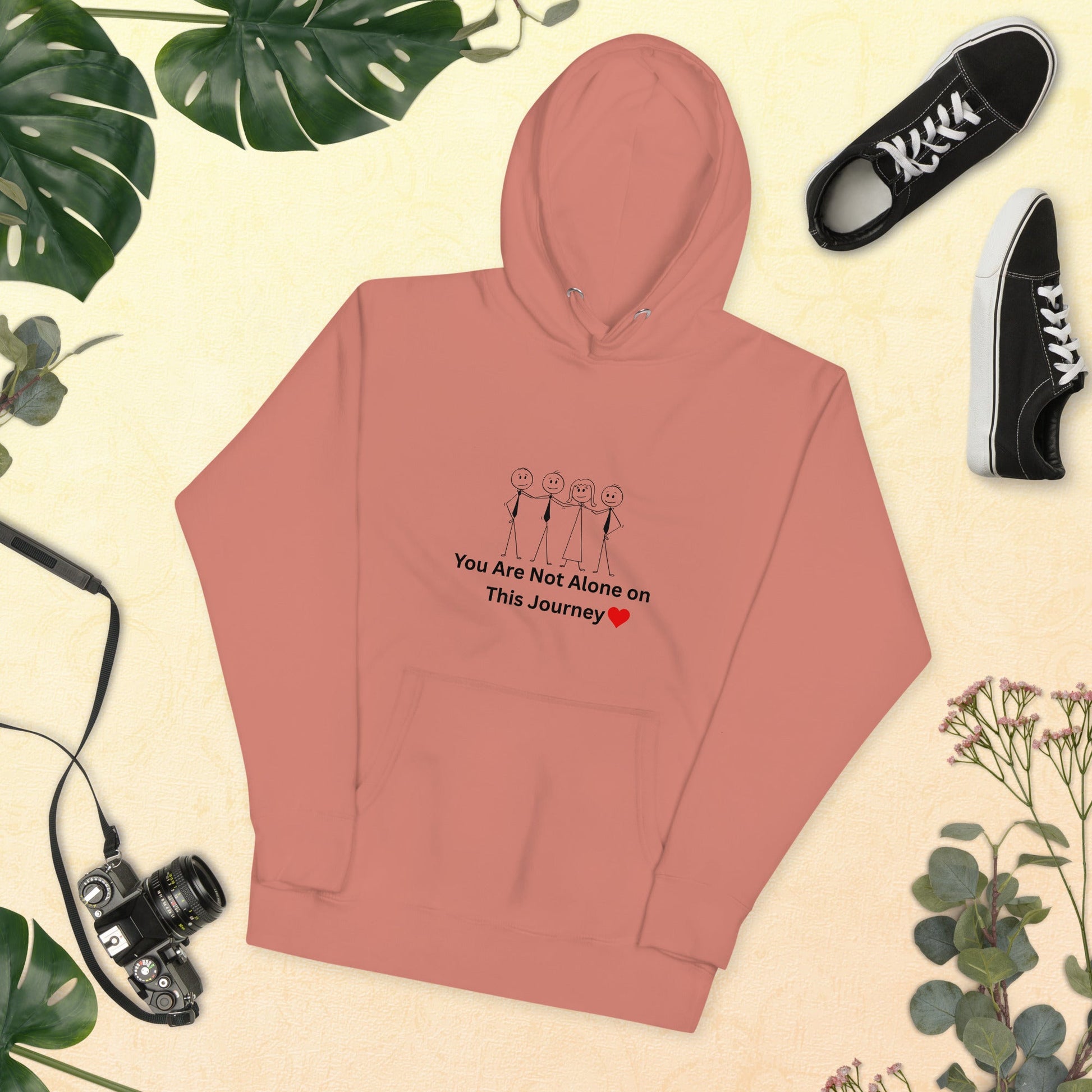 Pink hoodie with text and graphics on a beige background with shoes and plants.